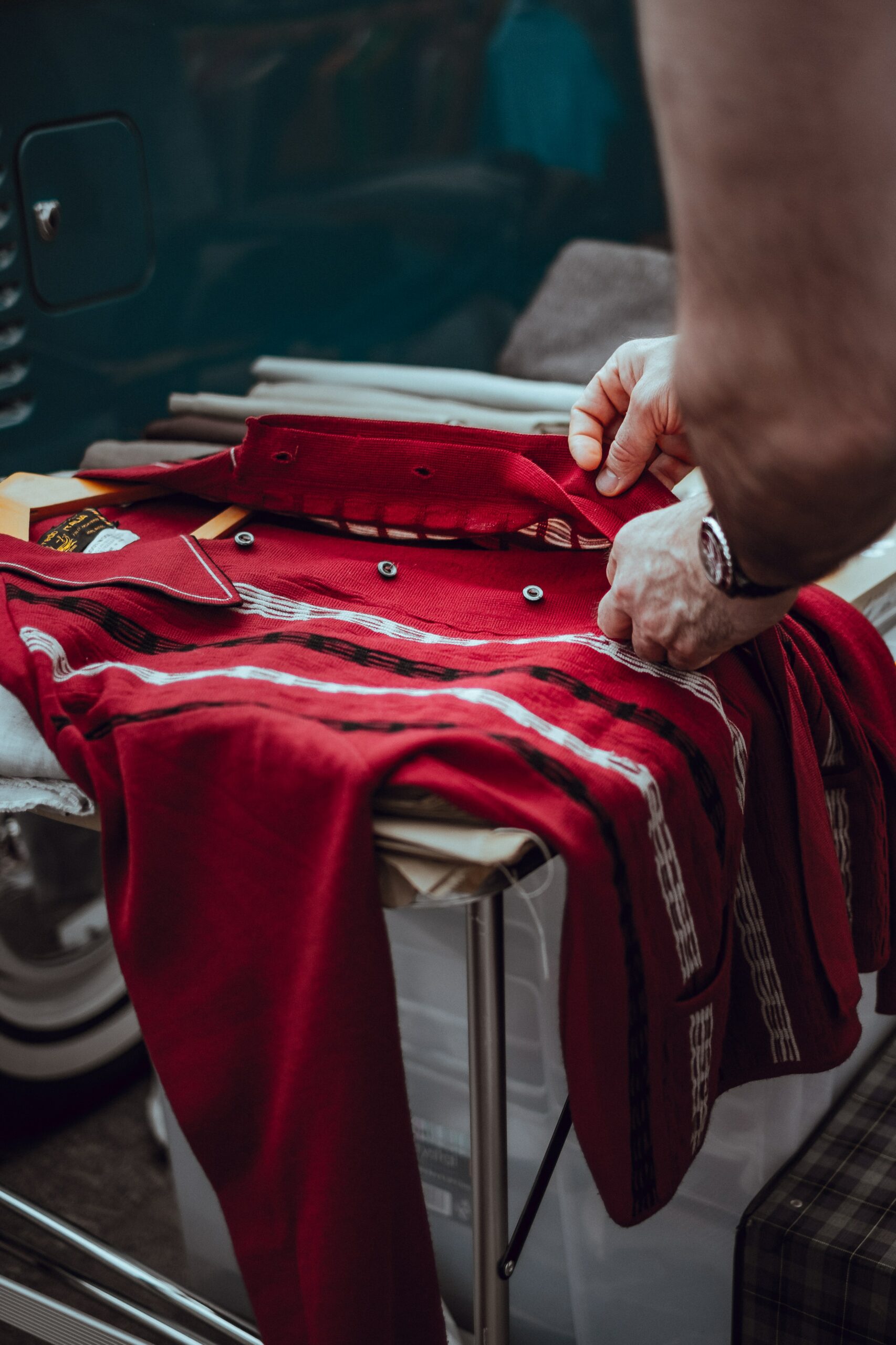 person holding red button-up dress shirt in second hand store