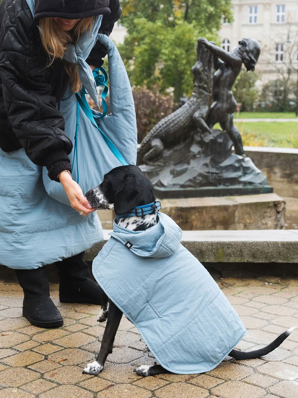 Winter Vegan Skirt Blue 3 Person in a long light blue skirt with a dog wearing a matching coat, standing in an outdoor setting with a statue in the background.