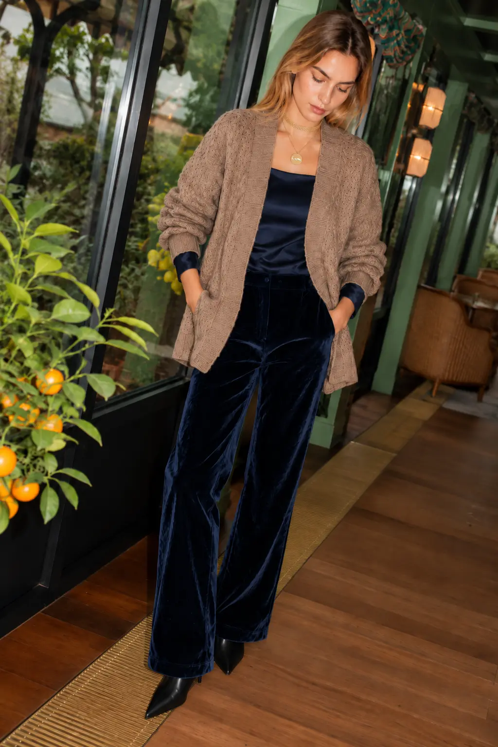 Woman in a hand-crocheted baby alpaca cardigan over a navy top with navy velvet trousers and fine jewelry